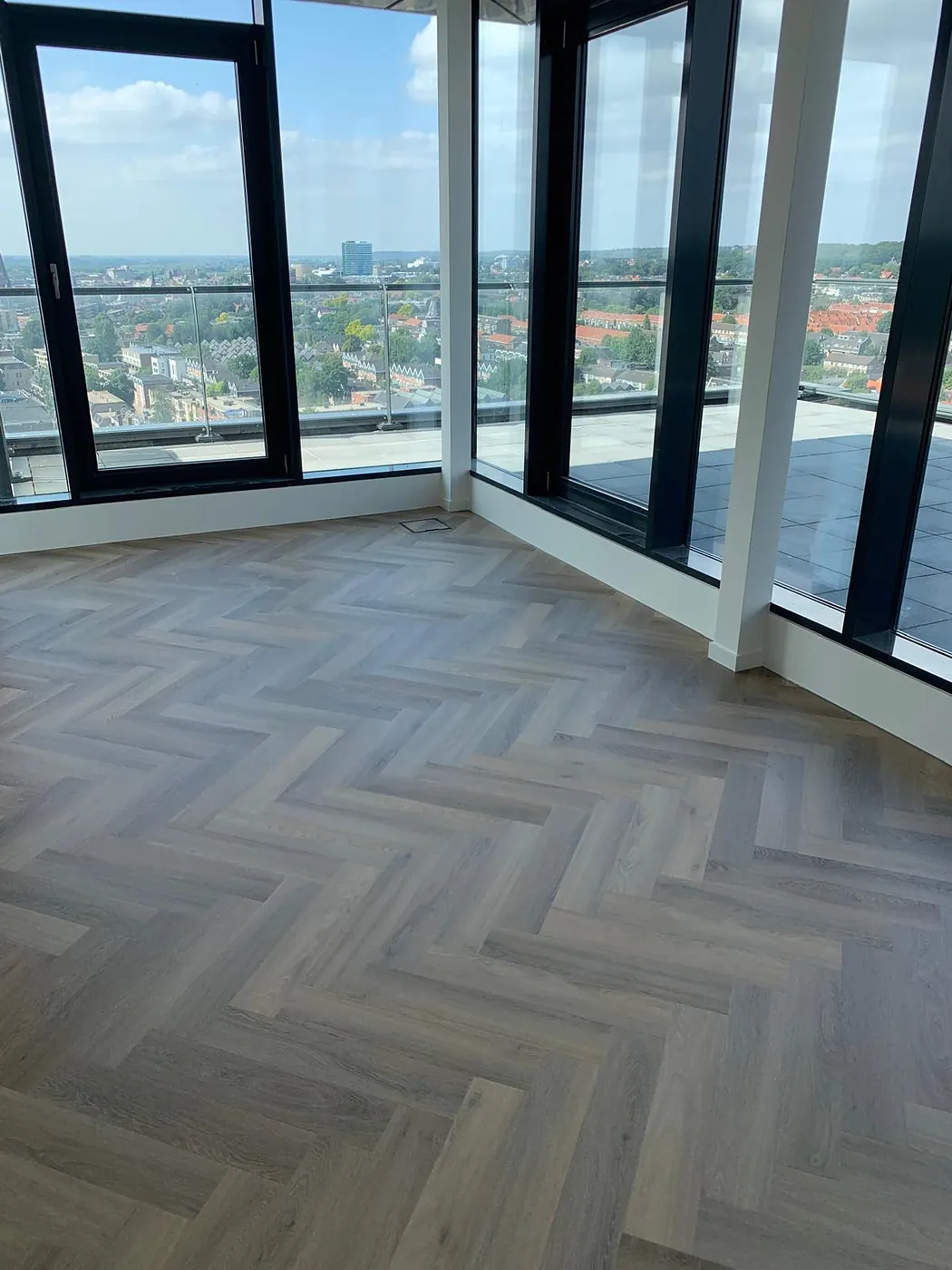 Lichtgrijze eiken visgraatvloer in een licht appartement met panoramisch stadsuitzicht