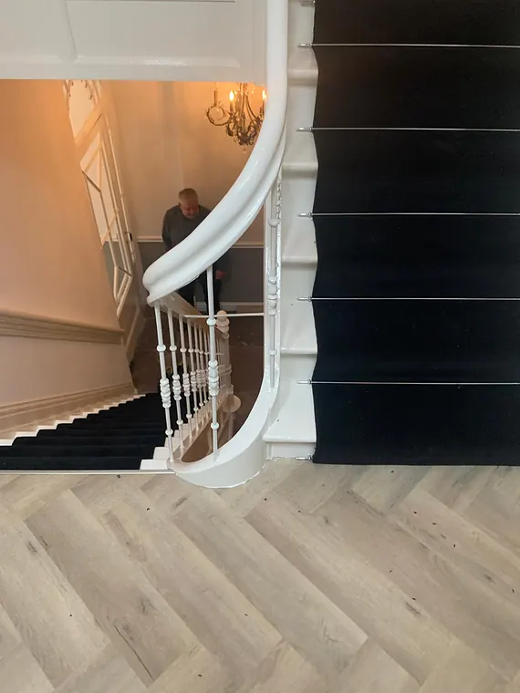 Zwarte traploper op een klassieke witte trap met grijze visgraatvloer