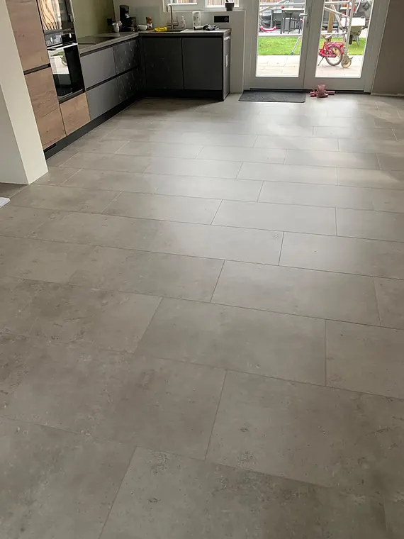 Grote lichtgrijze betonlook tegelvloer in een open woonkeuken met tuindeuren